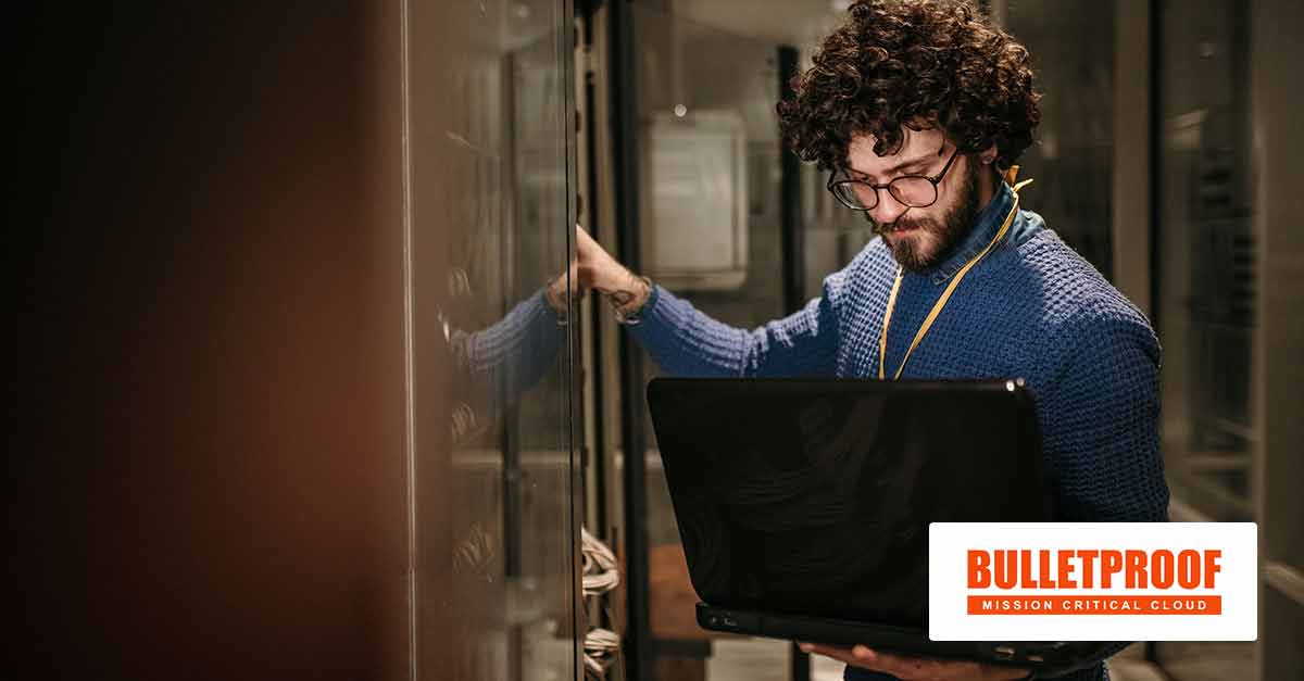 Young man standing in a server room with his laptop computer