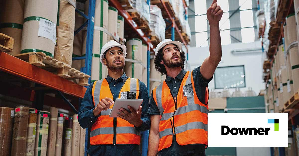 Two workers in a warehouse holding digital tablet with hardhat and safety vest