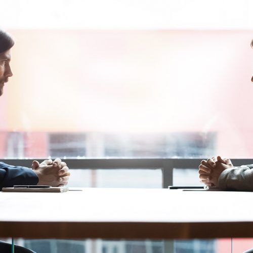 Two businessmen sitting opposite at table, confrontation and negotiation