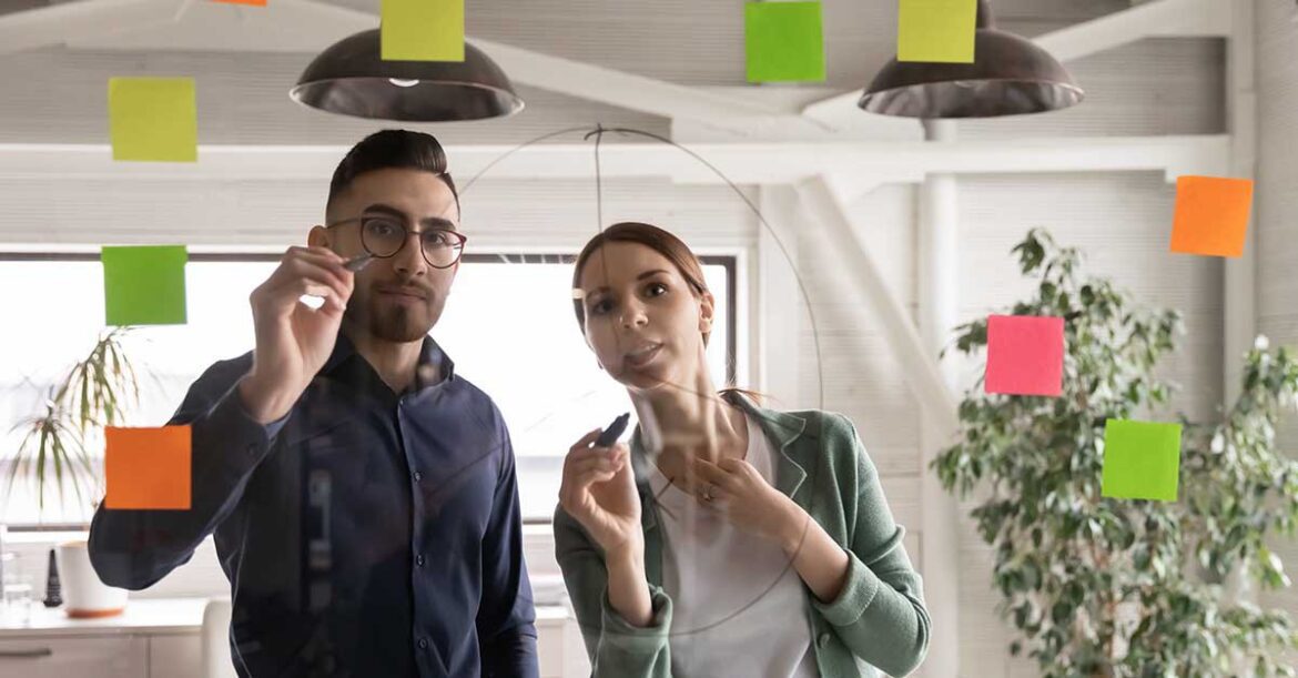 Two colleagues drawing a diagram on a glass window with post-it notes