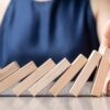 Business woman hand stopping falling wooden dominoes