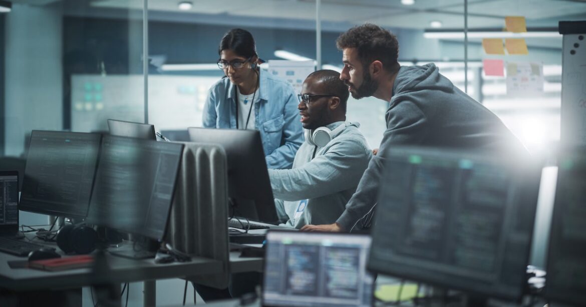 Agile delivery professionals with an IT colleague looking at computer screen